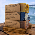 Stack of Rosanov Fire Bar, Hollander Ice Bar, and I'm Coming to the Cottage Bar soaps with a scenic background.