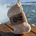 Soap bag with a label on a wooden surface with a blurred waterfall background