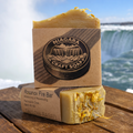 Two bars of soap with 'Niagara Craft Soaps' branding on a wooden surface with a scenic background.