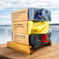 Stack of soap bars with visible branding on a wooden platform by a scenic waterfront.