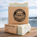 Two bars of soap with 'Niagara Craft Soap' packaging on a wooden surface with a blurred natural background.