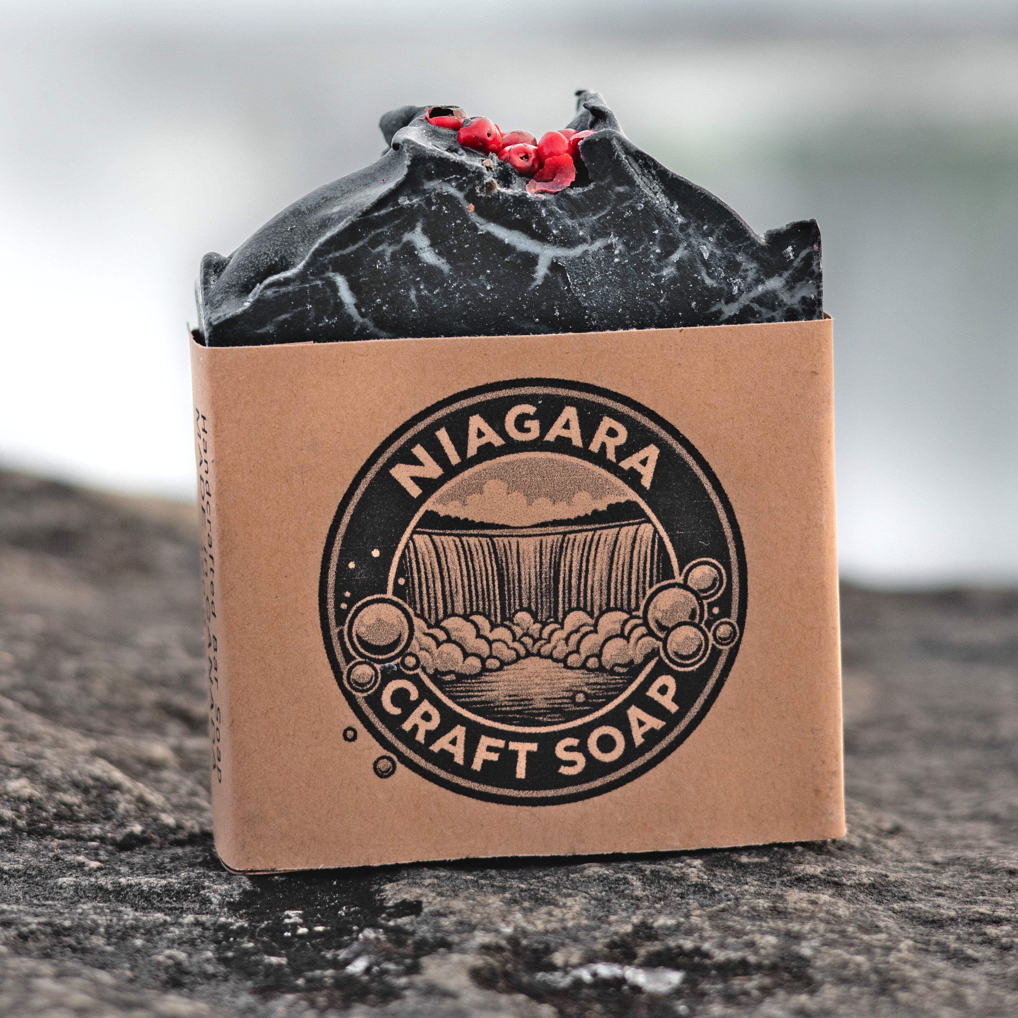 Niagara Craft Soap Charcoal Tallow Bar sitting on stone in front of Niagara Falls with label and logo Photographer Kurt Casucci.